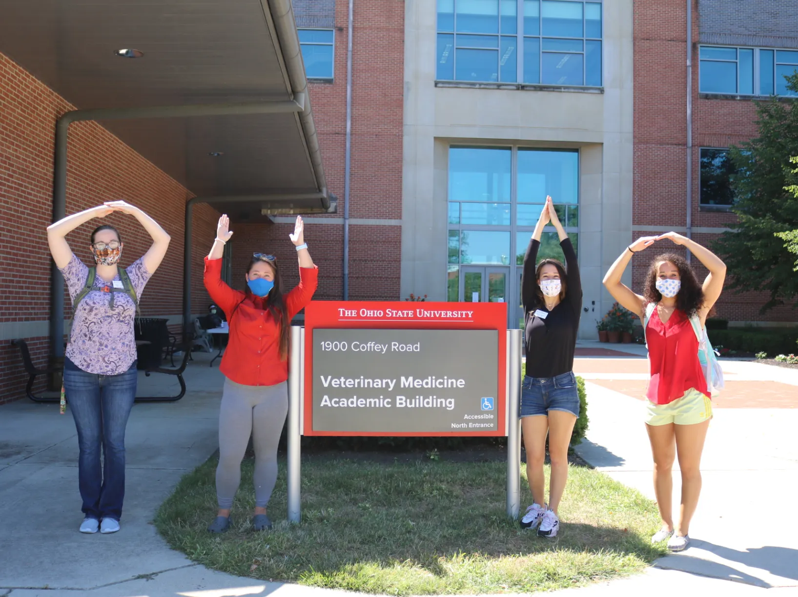 Four students posing in front of the Veterinary Medicine Academic Building sign