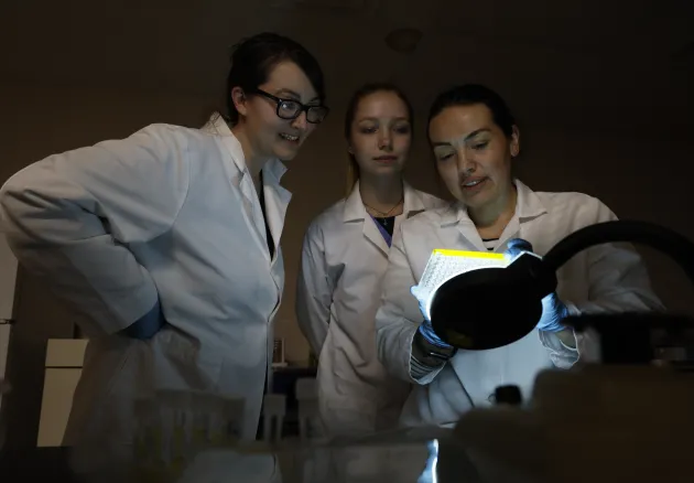 three female researchers in white coats looking at lab sample